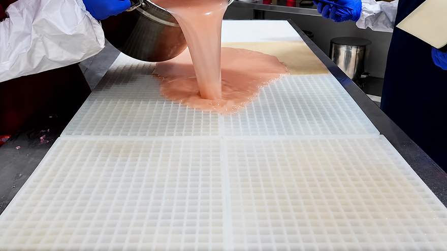 Team Gummy Molds che versa la miscela per caramelle gommose su un grande stampo commerciale in silicone prima della raschiatura