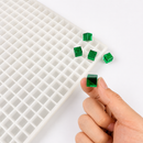 Hand holding a translucent emerald green 1mL cube gummy beside the silicone mold